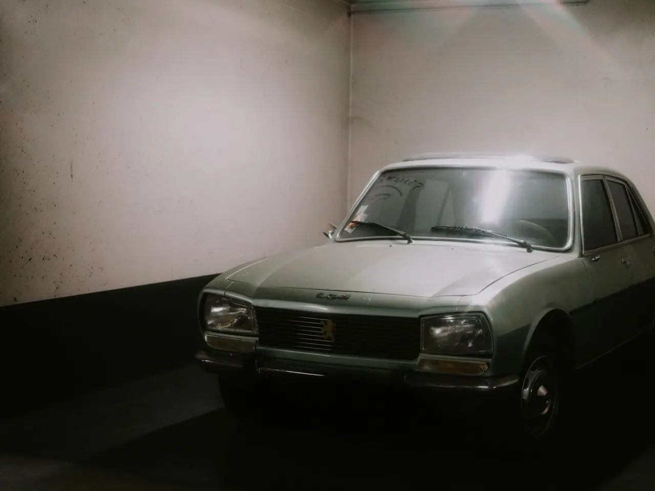 A classic silver sedan lit by a single lamp in a quiet indoor garage