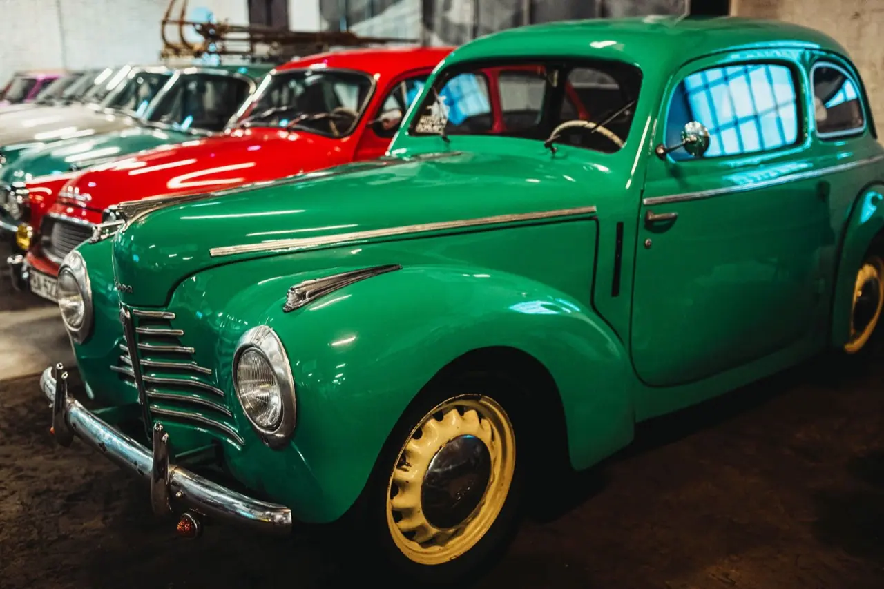 Vintage cars in green and red parked side by side inside a garage