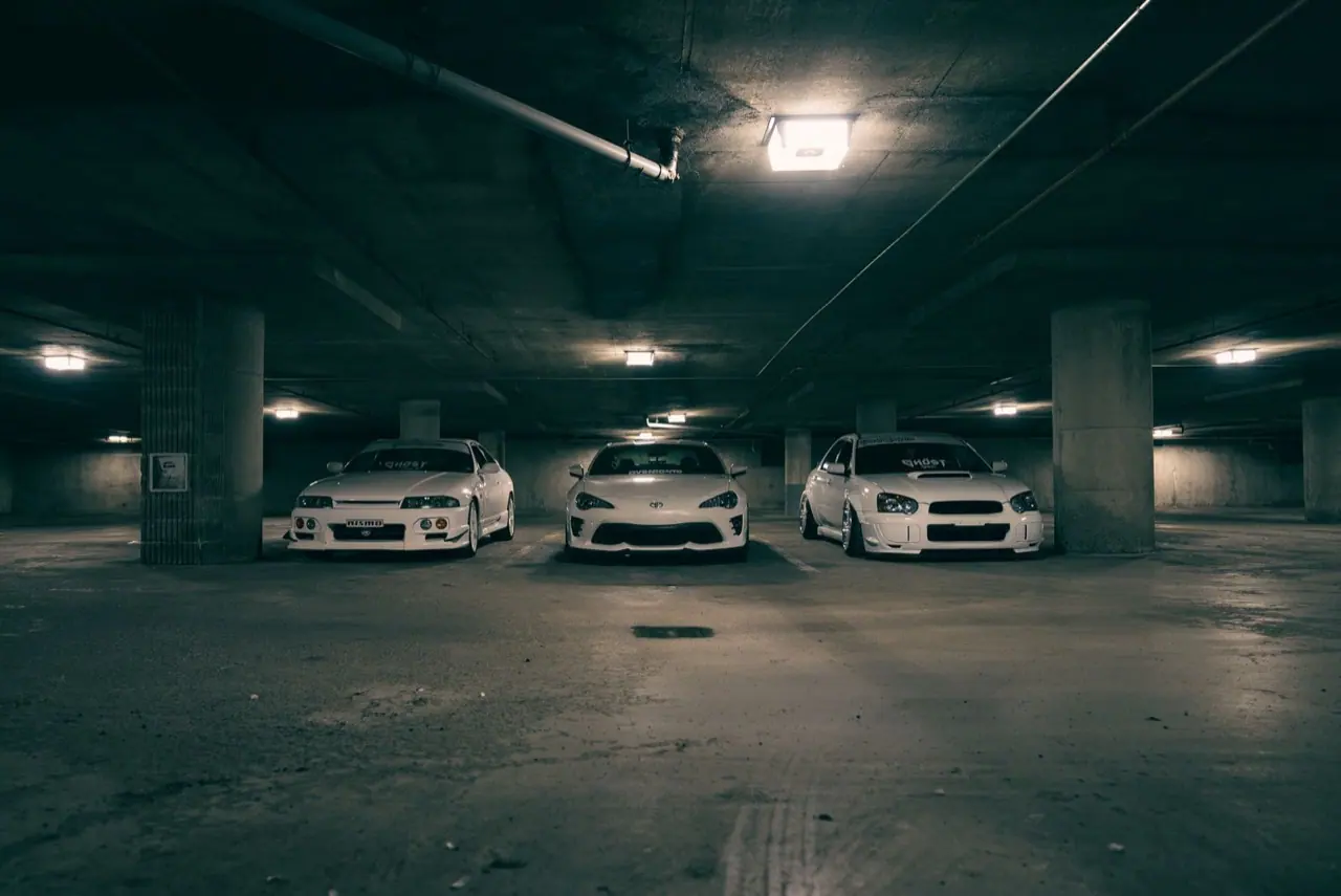 Three cars parked under the lights of an underground garage