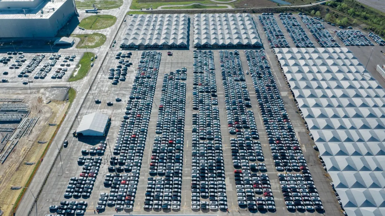 Rows of cars parked in a large outdoor vehicle storage lot seen from above