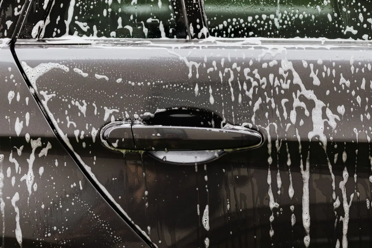 Soap suds running down the door of a black car during a hand wash