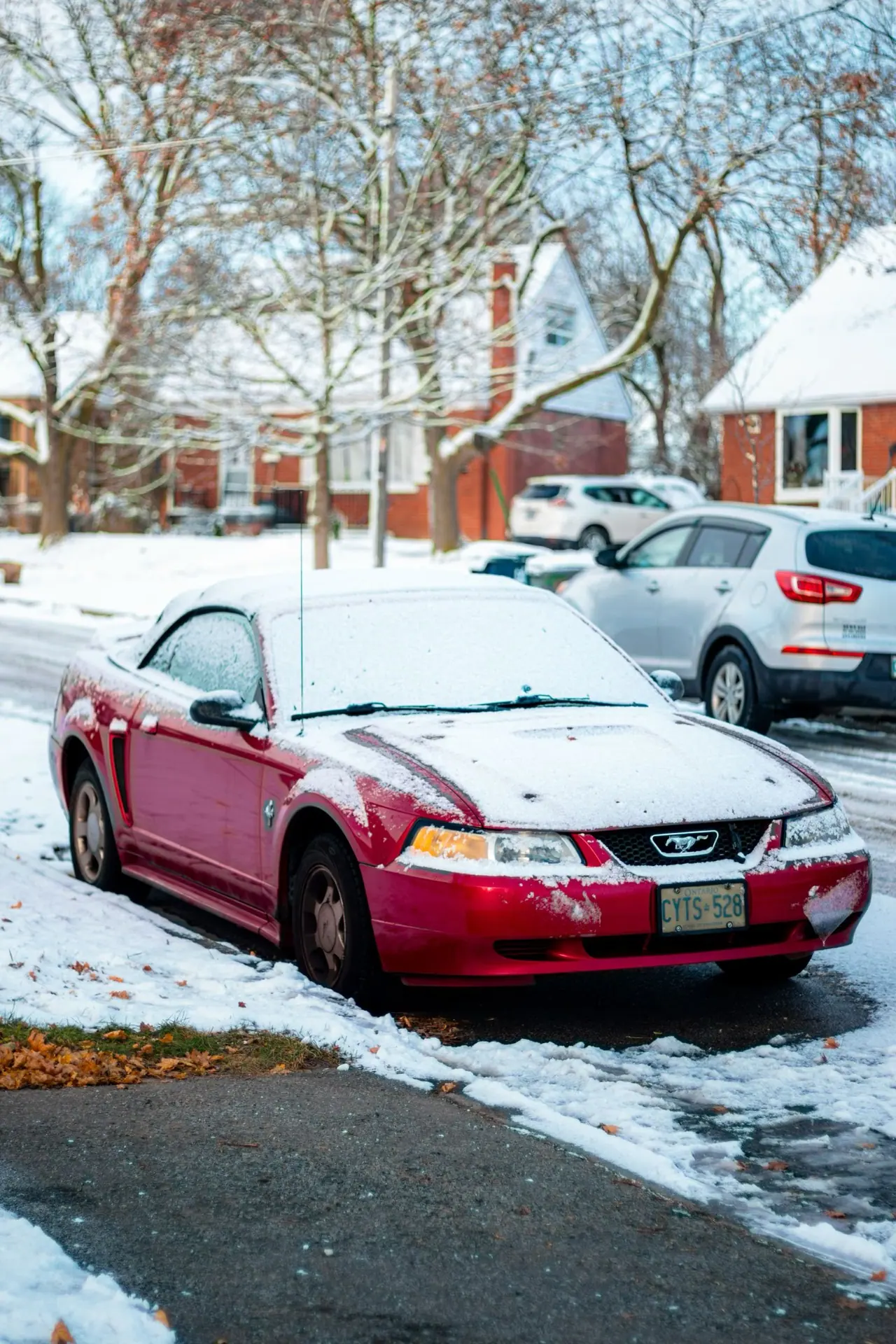 A red car parked on a snowy residential street in Toronto