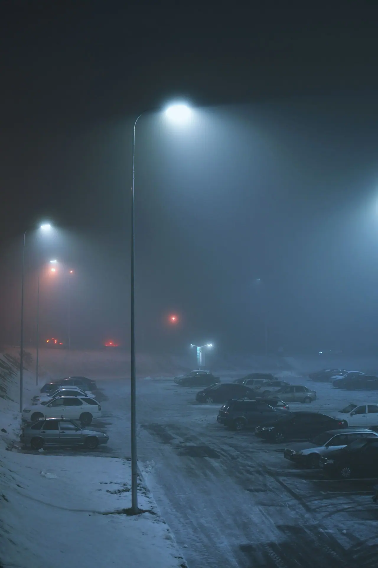 Cars in a snowy parking lot at night under a street lamp